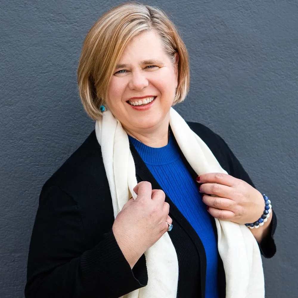 Maria Gudelis laughing, wearing a blue sweater and cream scarf
